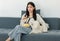Asian young happy cheerful female owner sitting smiling on cozy sofa couch holding eating popcorn glass bowl snack watching movie