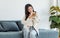 Asian young happy cheerful female owner sitting smiling on cozy sofa couch playing hugging cuddling with best friend small