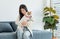 Asian young happy cheerful female owner sitting smiling on cozy sofa couch playing hugging cuddling with best friend small