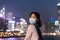 Asian young lady with face mask, blurred Colorful magnificent Night city view of Central, Hong Kong in background
