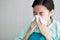 Asian young long hair unwell female patient wears green hospital uniform covered by blanket hold white tissue paper napkin in