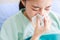 Asian young long hair unwell female patient wears green hospital uniform covered by blanket hold white tissue paper napkin in