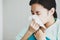 Asian young long hair unwell female patient wears green hospital uniform covered by blanket hold white tissue paper napkin in