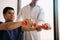 Asian young male physiotherapist helping patient with lifting dumbbells exercises in office