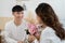 Asian young man kneeling and giving a bouquet of pink flowers to his girlfriend