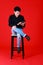 Asian young man smart and handsome sitting on chair folded leg and hold tablet on hand. Shooting at studio with isolated red