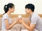 Asian young man and woman holding coffee cup on the bed. The lover smile and look at each other face happily