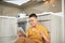 Asian young man work at home, an owner of online business, eating .sausage and looking on tablet