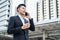 Asian young smart businessman talking telephone in city. The man holding phone and coffee walking outdoor to working office with s