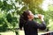 Asian young woman in black sportwear Thirsty and resting for drinking water in bottle after exercise and running with natural