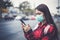 Asian Young woman using smart phone in the city wearing face mask because of air pollution, particulates and for protection flu