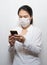 Asian young woman using smart phone wearing face mask protect air pollution, particulates and for protection flu.Coronavirus