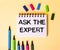 ASK THE EXPERT written in a white notebook on a beige background near multi-colored markers