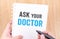 Ask your doctor word on white ring binder notebook with hand holding pencil on wood table,Health card concept