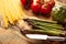 Asparagus, and an artichoke a sprig of tomatoes and sweet red pepper and Italian spaghetti on a cutting board with a knife, sliced