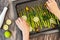 Asparagus, sliced lemon, olive oil, olives, mint leaves, rosemary, and some seasoning close up on baking sheet, woman hands.