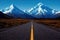 Asphalt empty road beyond horizont and high snow-capped mountains