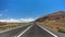 Asphalt road disappearing over the horizon through volcano mountain hillsides. White clouds on a blue sky. Lanzarote