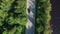 Asphalt road with driving cars through green summer forest near lake. Aerial shot from drone