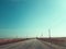 Asphalt road through the field under the electric wires. Power lines pass through brown fields