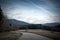 Asphalt road among fields, forests and mountains