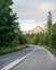 Asphalt road in forest, coniferous trees on both sides, mount Krivan peak Slovak symbol with afternoon sun clouds, in