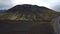 Asphalt road going by a green moss-covered volcanic mountain and black lava field in Iceland