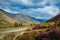 Asphalt road in mountains. Picturesque view of blooming hills and colorful sky with clouds. Straight paved road with white surface