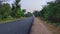 Asphalt road in rural area of India with grunge on edges closeup. Paved road leading to the village and White clouds in the sky