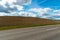 An asphalt road section in a rural area passing by agricultural fields against a background of blue sky and white fluffy clouds on