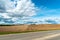 An asphalt road section in a rural area passing by agricultural fields against a background of blue sky and white fluffy clouds on