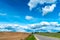 An asphalt road section in a rural area passing by agricultural fields against a background of blue sky and white fluffy clouds on