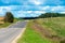 An asphalt road section in a rural area passing by agricultural fields against a background of blue sky and white fluffy clouds on