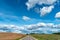 An asphalt road section in a rural area passing by agricultural fields against a background of blue sky and white fluffy clouds on