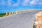 Asphalt road with stone guard barrier fence leading forward and right, blue sky white clouds