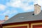 Asphalt shingles roof with skylights windows and rain gutter on the background of blue sky. House with old chimney.