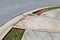 Asphalt street and concrete sidewalk with graded ramp between, green grass