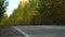 Asphalt Suburban Highway among a dense Autumn Forest on a Sunny Day. Cars pass quickly along the Winding Road. Concept