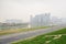 Asphalted road and sideway along river with city buildings in light winter mist