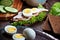 Assembling sandwich with meat, dark bread, fresh green salad, eggs and cucumbers on rustic wooden table surface