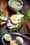 Assembling sandwich with meat, dark bread, fresh green salad, eggs and cucumbers on rustic wooden table surface