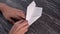 Assembling a white paper origami plane on a black textural wooden table