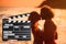 Assistant holding clapperboard and people kissing on beach at sunset. Cinema production