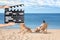 Assistant holding clapperboard and people relaxing in deck chairs on beach. Cinema production