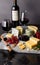 Assorted cheeses on black marble with green grapes and two glasses of red wine