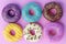 Assorted donuts with colorful icings on pink background.