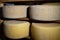 Assorted flavours of cheese wheels maturing on rows of wooden shelves in a cheese factory