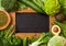 Assorted green toned raw organic vegetables next to vintage chalk menu board. Avocado, cabbage, cauliflower and cucumber with trim