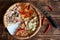 Assorted pizza, dried chilli peppers and cheese knife lie on a natural wooden surface of pine planks. Cut off a piece