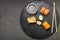 Assorted rolls on a black board next to sticks, soy sauce and ginger on a dark background.